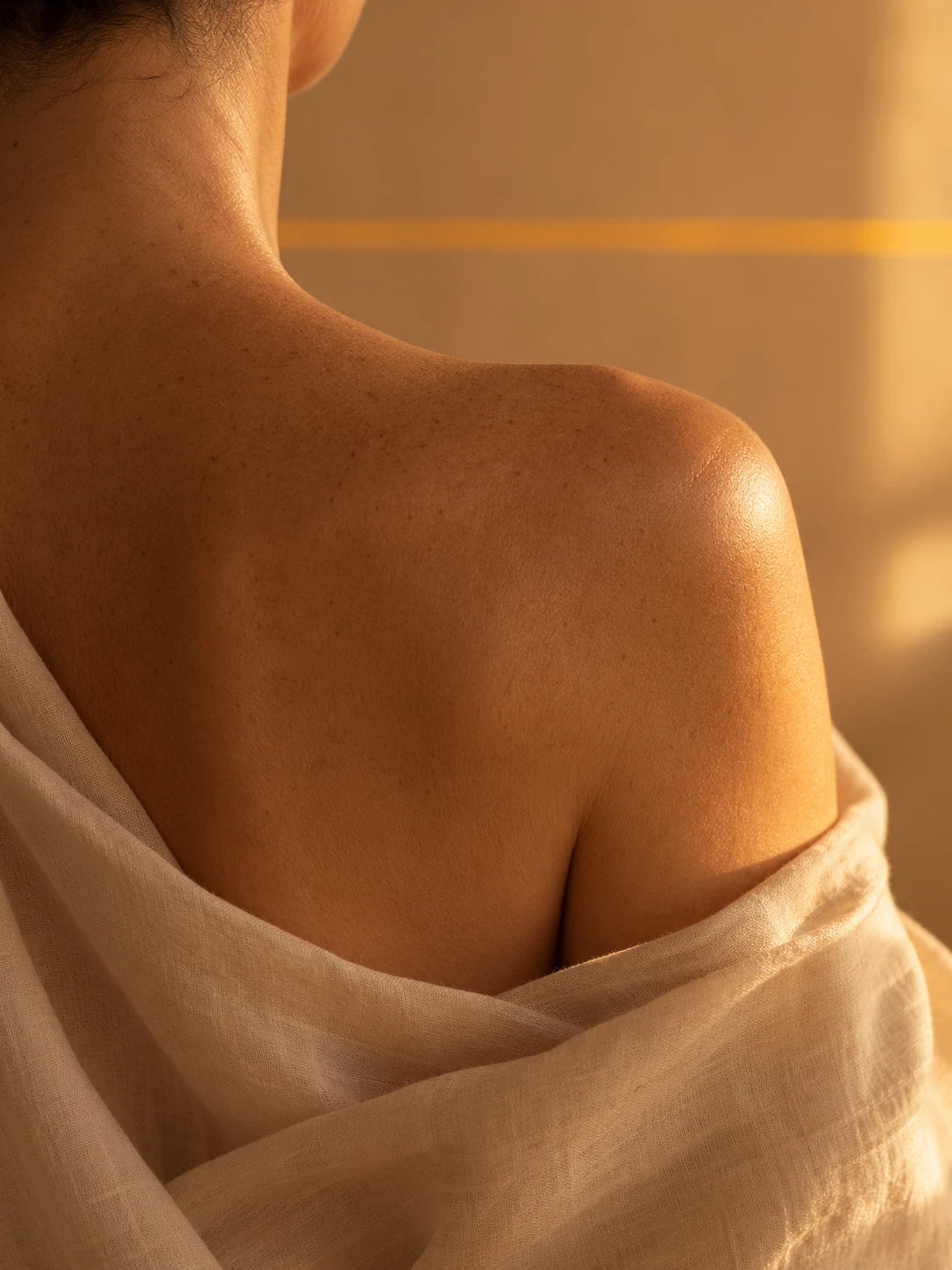 Back and shoulder of a woman in a sage olive linen robe in tungsten light