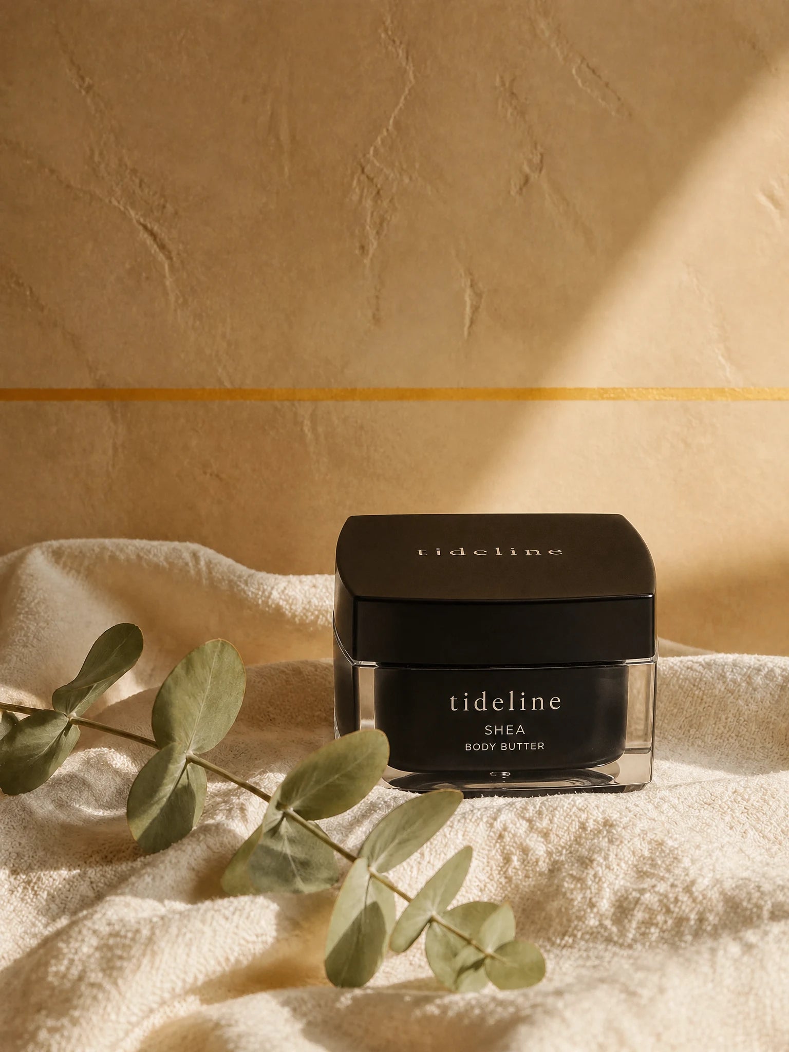 Tideline Shea Body Butter, a black square jar on warm linen in soft light