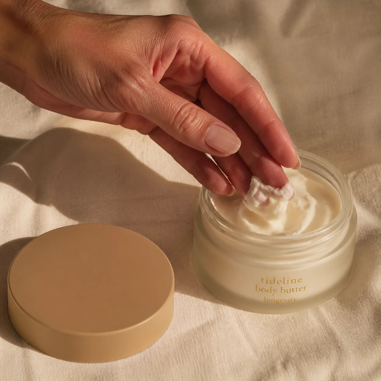 A hand scooping body butter from the Tideline jar